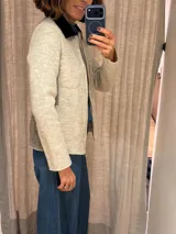 Chaqueta de lana hervida en color beige, con cuello en contraste color negro, cierre frontal metálico y bolsillos delanteros. Presenta un diseño estructurado con paneles laterales en tejido combinado.