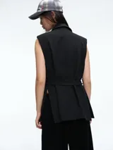 Chaleco sastrero negro de silueta estructurada, con solapas clásicas y lazo ajustable en la cintura. Presenta un diseño sin mangas con bolsillos laterales integrados.