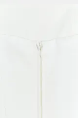 Top palabra de honor de tejido satinado blanco, con escote recto y diseño con bajo tipo peplum y costuras marcadas.