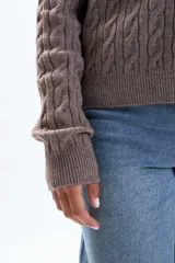 Saco de punto color tostado, con diseño de trenzas verticales en todo el cuerpo y mangas. Tiene cuello redondo y cierre frontal con botones pequeños.