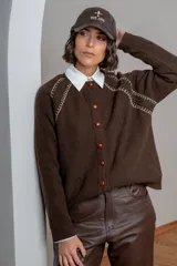 Saco de punto color marrón chocolate, con cierre frontal de botones en tono rojizo y detalle de costuras decorativas en color crema en la zona de los hombros y mangas.