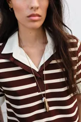 Top de estilo polo con mangas cortas, confeccionado en tejido de punto con diseño de rayas horizontales en tonos marrón y crema. Presenta cuello clásico y puños en contraste de color blanco en popelín, con cierre frontal de un botón y aberturas laterales en el bajo.