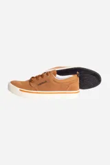 Zapatilla casual de cuero color camel, estilo skate o lona, con cordones marrones y suela de goma blanca con una línea naranja decorativa.