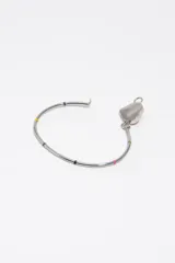 Pulsera rígida de metal dorado con dije central en forma de corazón esmaltado en negro y rodeado de letras de colores. Presenta pequeños detalles esmaltados de colores a lo largo del aro.