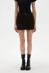 Falda mini de jean color marrón oscuro, con diseño de cinco bolsillos, cierre frontal con botón y costuras a tono.