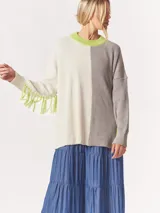 Buzo tejido oversized con bloques de color blanco y gris, cuello redondo en verde neón, tajos laterales y flecos verdes en las mangas.