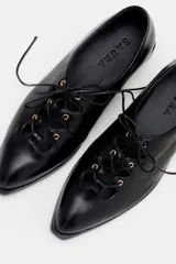 Zapato acordonado de cuero color bordó, con punta fina y diseño estilo oxford. Presenta cordones al tono y detalles de ojales metálicos dorados.