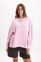 Buzo rosa de corte holgado y diseño liso, con cuello redondo, mangas largas y puños ajustados.