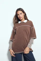 Remera de manga corta color marrón con efecto desgastado, corte oversize y costuras a la vista en color blanco. Presenta cuello redondo con cuello polo blanco superpuesto y mangas largas a rayas horizontales marrones y blancas por debajo.