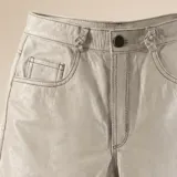 Pantalón flare de cuero vacuno en color hueso, con tiro alto y diseño ajustado con abertura en los tobillos.
