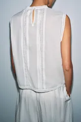 Blusa sin mangas de algodón con cuello redondo, diseño con paneles verticales bordados y detalles de encaje, cierre posterior con abertura y botón.