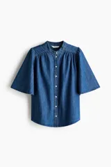 Blusa de denim de algodón suave, de color azul, con cuello mao, botonadura frontal y mangas cortas abullonadas.