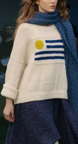 Sweater de tejido de punto color crudo, con diseño de la bandera de Uruguay bordado en el frente. Presenta cuello redondo, mangas largas con puños doblados y un calce holgado.