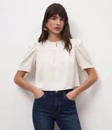 Blusa cropped de satén color crema, con cuello redondo, mangas cortas abullonadas con hombreras y detalle de fruncido en el frente.
