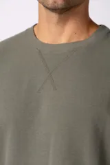 Remera de corte oversized en color marrón, confeccionada en tejido de algodón con textura de micropanal. Presenta cuello redondo con detalle de costura en forma de X y mangas cortas de estilo caído.