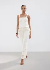 Pantalón palazzo color blanco con detalles bordados en el bajo de las piernas, tiro medio y cintura elástica con cordón ajustable.