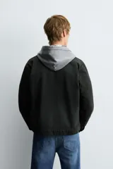 Sobrecamisa de denim de algodón negro con efecto lavado, corte relajado (relaxed fit). Presenta cuello solapa, cierre frontal con cremallera, manga larga con puño abotonado y bolsillo plastrón en el pecho.