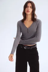 Top de manga larga en tejido de punto acanalado fino, color gris oscuro. Presenta un escote en V pronunciado con una pequeña abertura central cerrada con corchetes.