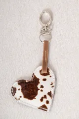 Llavero en forma de corazón confeccionado en cuero con pelo estampado tipo animal print, con tira de cuero lisa y gancho metálico.