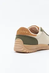 Zapatilla urbana de mujer con silueta retro, combinando paneles de cuero blanco y gamuza gris claro. Posee un talón trasero en gamuza negra y suela robusta de goma color caramelo con relieve.