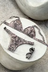 Bikini de dos piezas color marrón, con corpiño triangular fijo con corte bajo el busto, breteles regulables con hebilla y almohadillas desmontables. La bombacha es vedetina con frunce elástico en los costados.