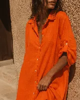 Vestido camisero corto de lino, de corte amplio y cómodo, con diseño irregular más largo en la parte trasera. Presenta mangas arremangables con presilla y botones, cierre frontal con botones de nácar y cuello camisero.