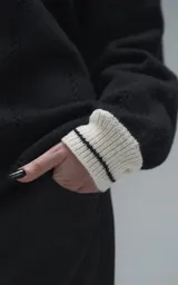 Sweater de punto negro con cuello polo en color crema, manga larga y diseño oversize. Presenta bordados en el frente con la inscripción 'Ravers', el número '90' y letras cursivas, con terminaciones en punto rib en puños y cuello.