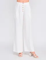 Pantalón palazzo color blanco, confeccionado en mezcla de lino y viscosa, de tiro alto con cierre frontal de botones, pinzas en la cintura y piernas anchas.