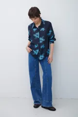 Camisa de corte clásico con cuello camisero y cierre frontal de botones, confeccionada en tela color bordó con estampado floral en tonos celestes.