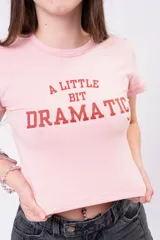 Remera baby tee color rosado, al cuerpo, de manga corta, con estampa frontal en tono rojo con la leyenda "A little bit dramatic".