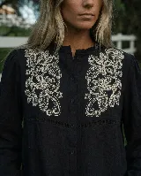 Camisa marrón chocolate de manga larga con bordado artesanal floral en hilo crudo sobre el pecho. Cuenta con cuello con sutil volado, cierre frontal de botones y mangas abullonadas con puños ajustables.