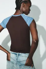 Camiseta de manga corta estilo raglán, con cuerpo principal marrón oscuro y mangas cortas en color celeste claro. Presenta cuello redondo con costuras a contraste.