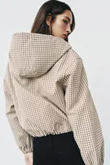 Campera estilo cazadora con capucha ajustable con cordones, cierre frontal de cremallera, mangas largas con puños elásticos, bolsillos delanteros de doble vivo y bajo ajustable con cordones. Presenta un diseño de cuadros en tonos beige y marrón.