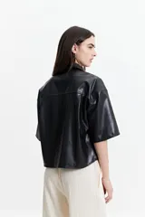 Camisa de manga corta confeccionada en cuero sintético color bordó, con cuello clásico, cierre frontal de botones metálicos y dos bolsillos frontales con solapa.