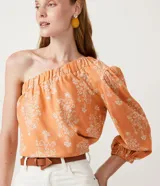 Blusa color durazno con estampado floral blanco, con un solo hombro y manga larga abullonada.