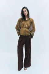 Pantalón cargo de tiro medio en color marrón oscuro, con corte recto y amplio. Presenta bolsillos laterales tipo cargo con solapa y detalle de pliegues frontales. Cierre frontal con cremallera y botón.