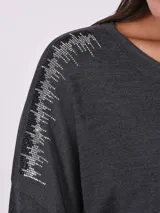 Blusa de manga larga en color rosado, con cuello redondo y detalle de apliques brillantes en los hombros. Presenta un corte holgado y diseño básico.