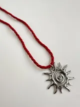 Collar con dije de acero quirúrgico en forma de sol con centro en espiral y cordón de tela trenzado en color rojo.