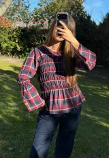 Blusa de manga larga con diseño a cuadros escoceses en tonos bordó, verde y azul. Presenta cuerpo con frunces elastizados y mangas amplias con puños acampanados.