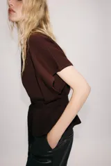 Chaqueta marrón de punto con cuello redondo y manga corta. Presenta cierre frontal con botones y un cinturón integrado del mismo tejido con lazo para atar en la cintura.
