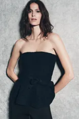 Top de punto sin mangas con escote recto, diseño ajustado al cuerpo y bajo con volado peplum. Presenta un detalle de lazo decorativo en la cintura.