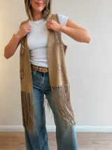 Chaleco marrón efecto gamuza, con diseño abierto sin mangas, apliques de crochet en relieve con motivos geométricos y florales, y flecos largos en el ruedo.