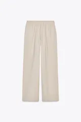 Pantalón negro de tiro alto con cintura elástica ajustable mediante cordones con terminales dorados. Presenta pernera ancha y bolsillos laterales. La tela tiene una textura sutilmente arrugada o plisada.