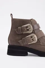 Botín de cuero vacuno color marrón, con punta fina y detalle de tachas metálicas en la parte superior. Presenta una suela de plataforma plana de color negro.