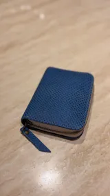 Billetera de cuero con textura grabada tipo reptil, color azul, con cierre perimetral y tirador de cuero a juego.
