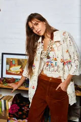 Camisa holgada color crema con bordados de palmeras y frutos, confeccionada en algodón. Presenta terminación de puntilla en el ruedo.