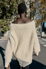 Jersey de punto con cuello barco y manga larga, confeccionado en tejido efecto cepillado. Presenta un diseño asimétrico en el bajo con detalle de encaje aplicado.