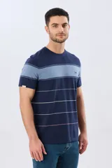Remera de algodón con diseño de rayas horizontales en tonos azul marino, celeste y líneas finas en verde claro y amarillo pálido. Cuenta con cuello redondo y mangas cortas, con un pequeño bordado en el pecho.