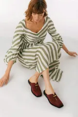 Zuecos de cuero color bordó con punta cuadrada, detalle de abertura en el empeine y aplique metálico dorado.