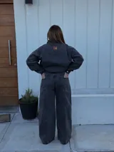 Pantalón de jean tiro medio con corte wide leg, color negro lavado, con bolsillos delanteros tipo cargo y costura vertical central en las piernas.